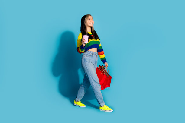 完整的照片可爱的年轻女士购物走拿咖啡穿着时尚的条纹服装孤立的蓝色背景图片下载