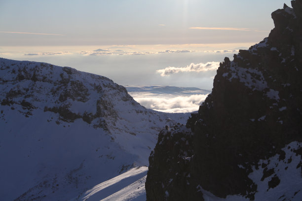 雄伟的山峰在云层之上，雪峰和日出时温暖多彩的天空。图片下载