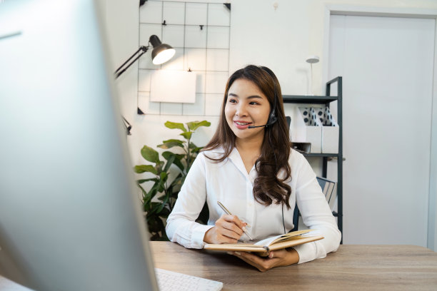 在现代办公环境中，带着耳机微笑的呼叫中心座席在办公桌前工作图片下载