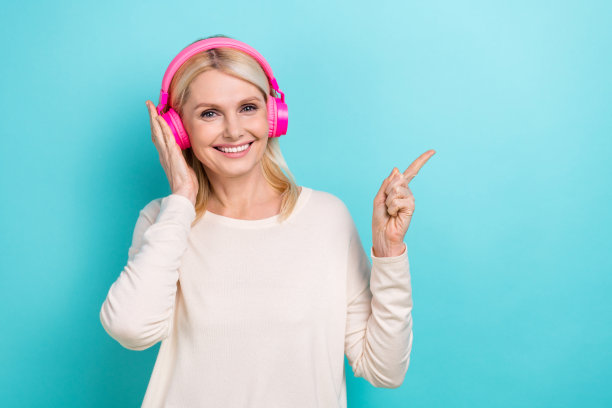 照片中退休年龄的金发女士穿着时尚的衬衫新的无线耳机直接手指空的空间spotify孤立在青色的背景图片下载