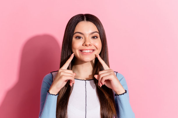 照片中开朗可爱的漂亮女孩穿着蓝色时尚的衣服，在粉红色的背景上露出牙齿图片下载