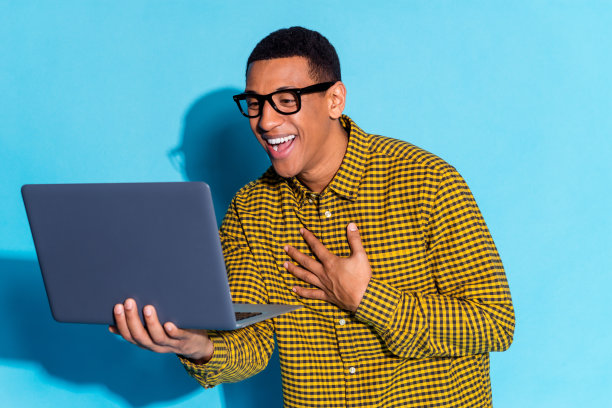 照片肖像英俊的年轻人拿着上网本视频电话笑穿着时尚的格纹服装孤立的蓝色背景图片下载