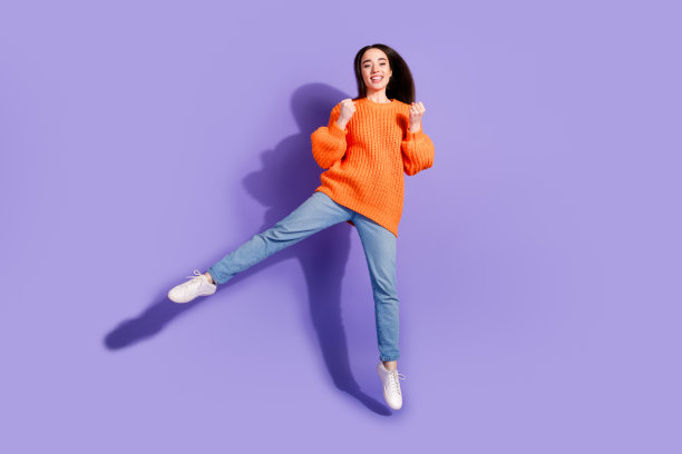 照片上开朗迷人可爱的女孩穿着时髦的衣服，双手握拳是飞空气孤立在紫罗兰色的背景图片下载