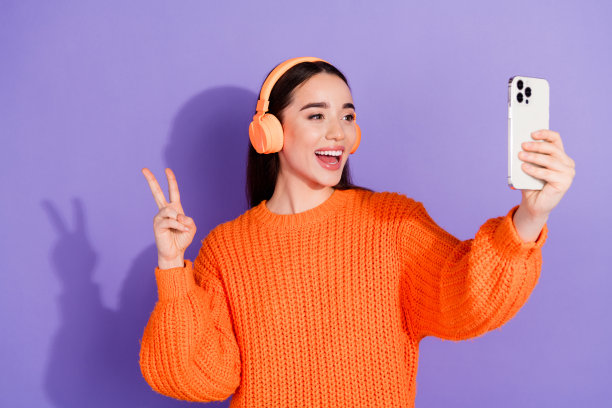照片中可爱可爱的女孩博主穿着时髦的橙色衣服，摄像头v字标志孤立在紫色背景上图片下载