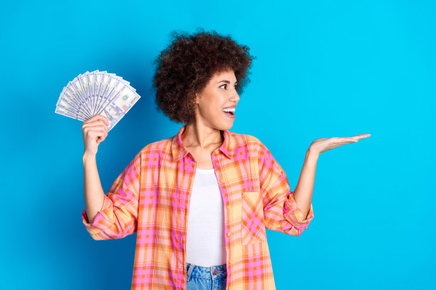 漂亮的年轻女孩的照片肖像拿着钱扇看空空间穿时髦的格子装孤立在蓝色的背景图片下载