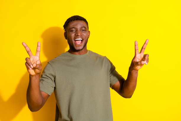 照片中，开朗开朗的帅哥穿着卡其色时髦的衣服，手臂上的v字标志孤立在黄色的背景上图片下载