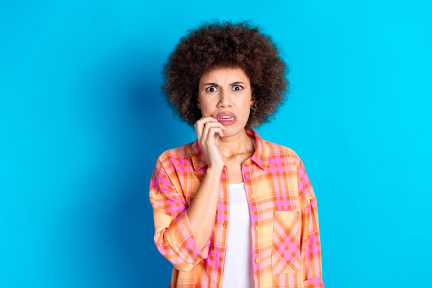 漂亮的年轻女孩的照片肖像咬指甲害怕穿时髦的格纹服装孤立的蓝色背景图片下载