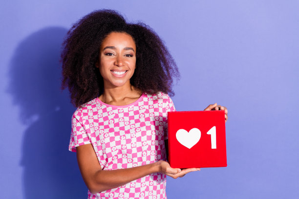 照片肖像迷人的年轻女子抱着心脏图标穿着时尚的粉红色衣服孤立的紫色背景图片下载