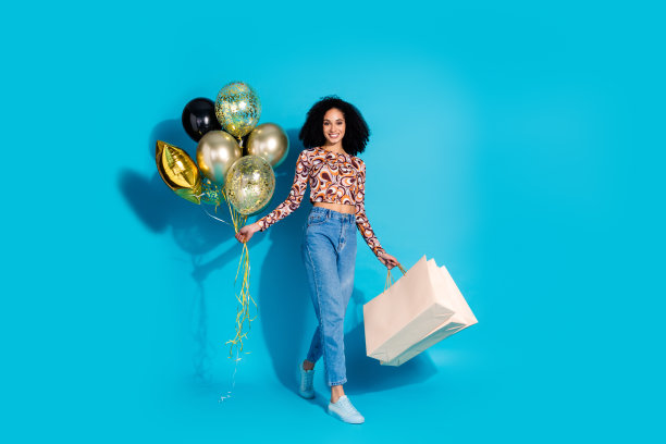 照片中，开朗可爱的女人穿着时髦的衣服，拿着气球走在蓝色背景的空旷空间里图片下载