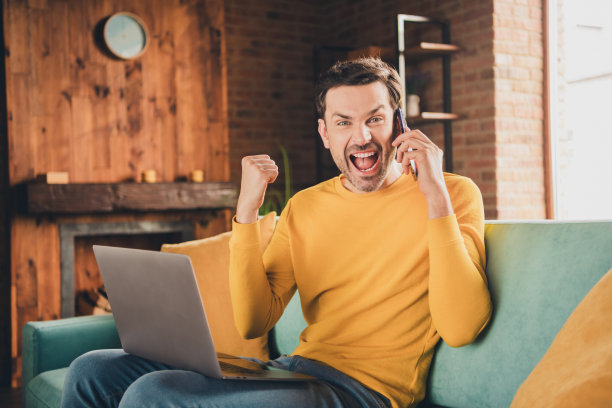 年轻人的照片肖像坐在沙发上网本讲电话赢穿着黄色的衣服花消遣宽敞的房子在室内房间图片下载