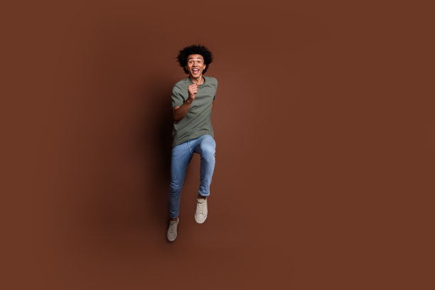 英俊的年轻男性跑步匆忙穿着时尚的卡其布服装孤立的棕色背景的全长照片图片下载