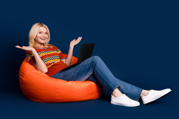 照片华丽漂亮的高级漂亮女人穿着时髦的衣服，坐在使用上网本孤立的深蓝色背景图片下载