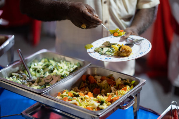 深色皮肤的手从素食自助餐中拿起食物放到盘子里。图片下载