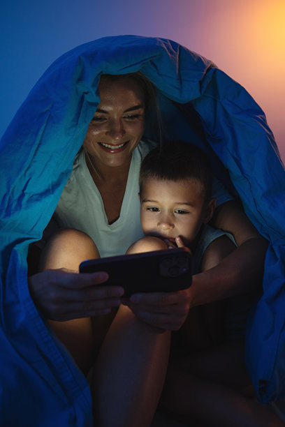 母亲和儿子晚上在床上一起看智能手机图片下载