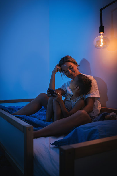 母亲和儿子晚上在床上一起看智能手机图片下载