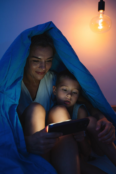 母亲和儿子晚上在床上一起看智能手机图片下载