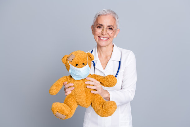 照片迷人的快乐儿科医生合格的专家穿着白色长袍拿着玩具孤立在灰色背景图片下载