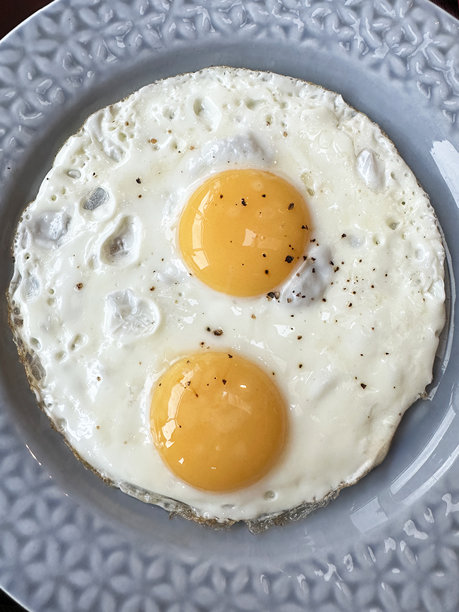 蓝色盘子的特写图片，有花卉图案的边缘，里面有两个煎鸡蛋，煎鸡蛋是用椒粉玉米调味的图片下载
