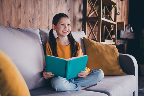 漂亮的小女孩的全身照片，坐在沙发上看书，穿着橙色的衣服，现代室内平坦的室内图片下载