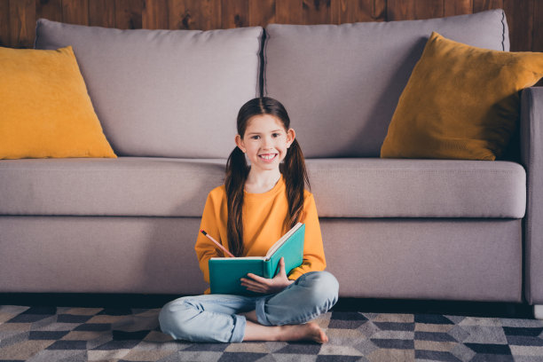 漂亮小女孩的全身照片坐在地板上写笔记本穿着橙色的衣服现代室内平坦的室内图片下载