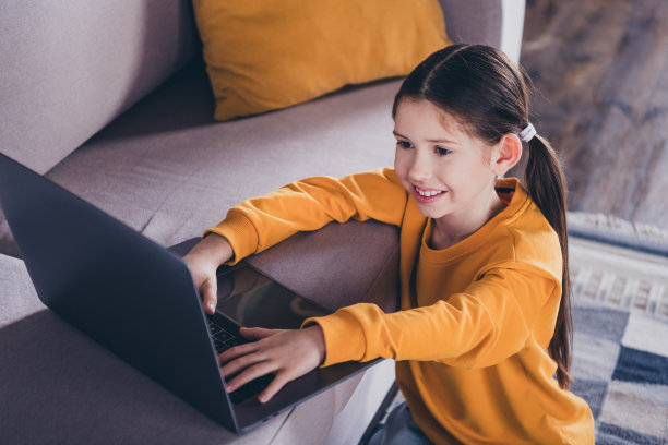 漂亮小女孩的照片肖像坐在地板沙发上网本穿着橙色的衣服现代室内平坦的室内图片下载