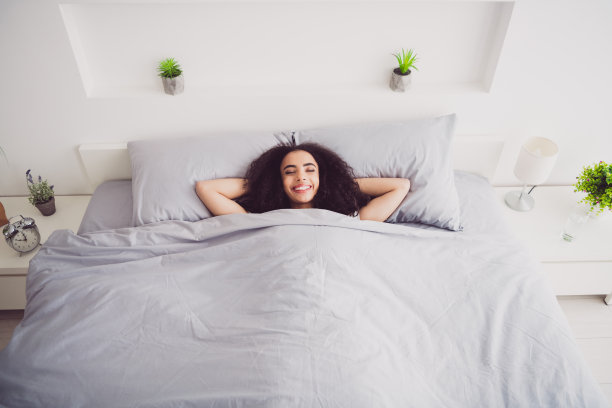 年轻迷人的女人躺在床上的照片，双手在头后面休息，穿着时尚的睡衣，柔软舒适的卧室，白色的房间内部图片下载