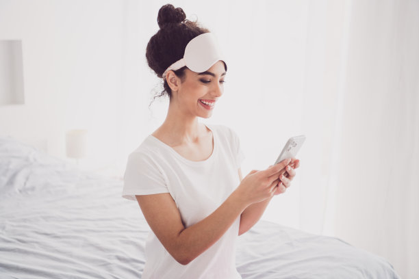 美丽的美国可爱的年轻女孩穿着睡衣的照片，早上醒来，早上好，舒适的卧室，大床，在室内浏览智能手机图片下载