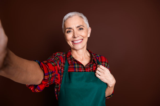照片正面可爱的高级女士穿着红色格子衬衫，在棕色背景下拍摄自拍图片下载
