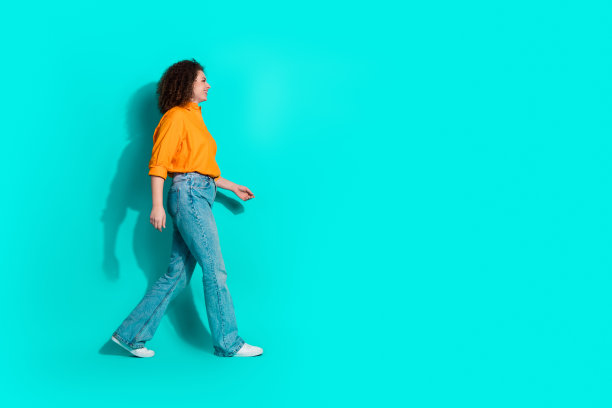 乐观的女人穿着橙色衬衫去购物的全尺寸照片，在蓝绿色的背景上看起来空无一物图片下载