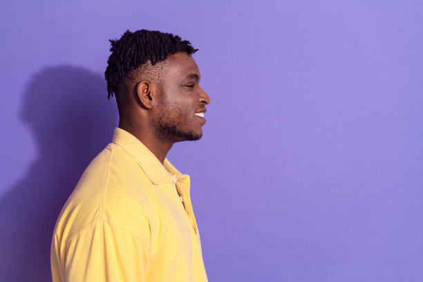 照片肖像的漂亮年轻的男性侧面看空空间穿时髦的黄色服装孤立在紫色的背景图片下载