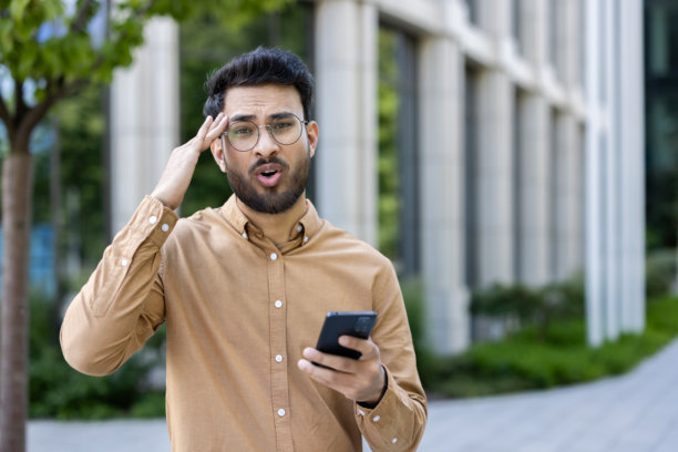 一名男子在办公大楼外接电话时拿着智能手机感到惊讶图片下载