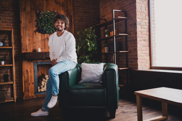 时髦酷的家伙穿着白色套头衫的照片，微笑着放松的家在室内的房子公寓房间图片下载