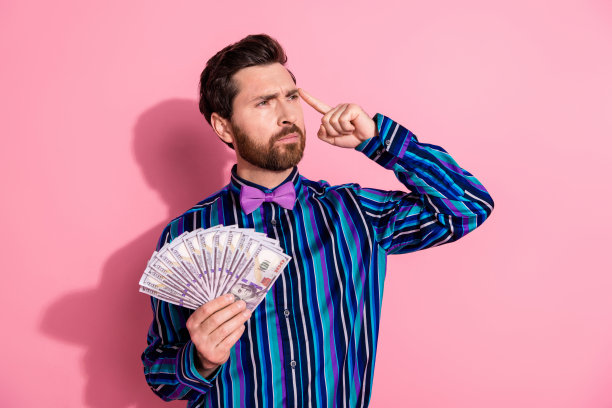 照片中沉思优雅的富人穿着时髦的条纹衣服，拿着钱现金，在粉红色的背景上看起来空无一物图片下载