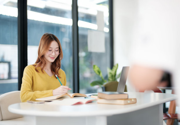 一个女人坐在书桌前，手里拿着一本书和一支笔图片下载