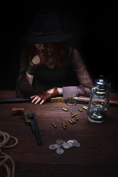 拿着左轮手枪的狂野西部女孩坐在桌子旁还有弹药和银币图片下载