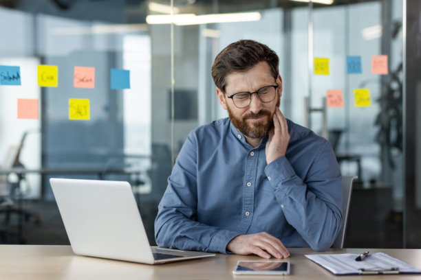 一名男子在办公室用笔记本电脑工作时牙痛图片下载