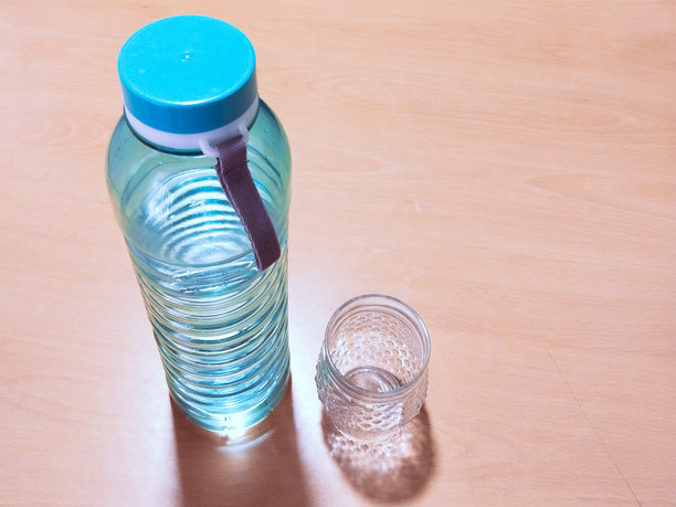 塑料水瓶与玻璃在木桌上，水瓶在光木表面，图像库存照片图片下载