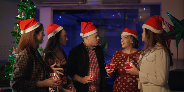 印度一群年轻的成年同事带着圣诞老人的帽子站在室内家庭办公室庆祝新年聚会。快乐的老年群体人们捧着杯子喝着酒，喝着果汁，一起享受欢乐图片下载