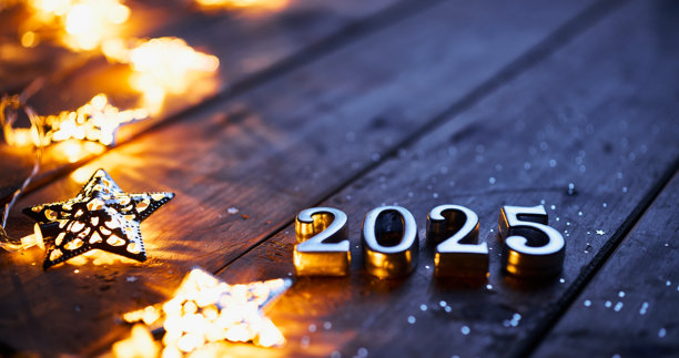 金属数字在木制表面形成“2025”，周围是发光的星形灯和散落的闪光，创造了一个节日和神奇的新年场景。图片下载