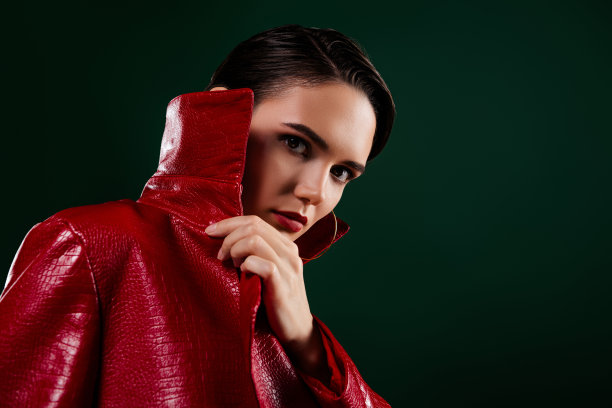 照片中迷人的女孩触摸覆盖近脸与红色大衣衣服隔离在深色背景图片下载