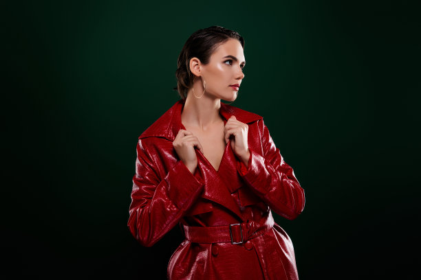 照片的黑发女孩摸她的红色皮夹克看侧面孤立的深绿色背景图片下载