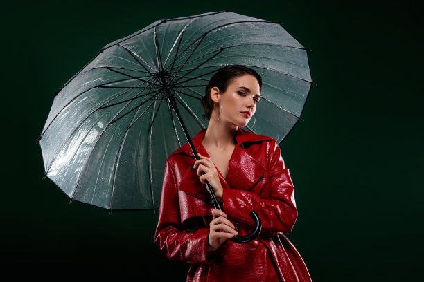 照片中迷人优雅的女孩穿着红色的时尚大衣，手持遮阳伞，孤立的深色背景图片下载