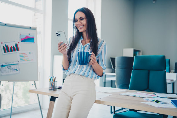 照片聪明的首席女休息手持设备喝咖啡穿条纹正装舒适的现代办公室室内室内工作空间图片下载