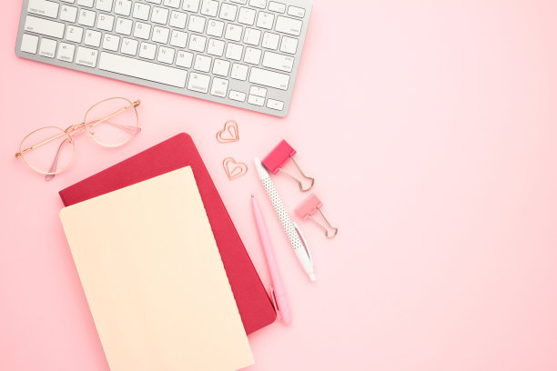 办公工作台的平面布局，键盘、眼镜、笔记本、夹在淡粉色背景上。在家办公，远程办公理念。图片下载