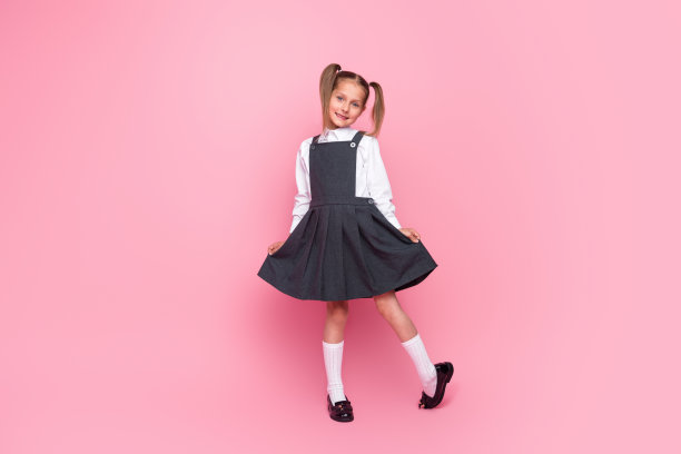 可爱的小女生的全身照片勤奋摆姿势展示裙子穿着时尚的制服孤立在粉红色的背景图片下载