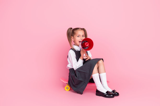 小女生的全身照片骑滑板宣布扩音器穿着时尚的制服孤立在粉红色的背景图片下载