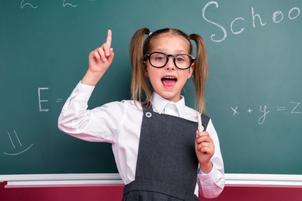 照片中可爱的小女生兴奋的点了起来，尤里卡穿着时尚的校服教室黑板背景图片下载