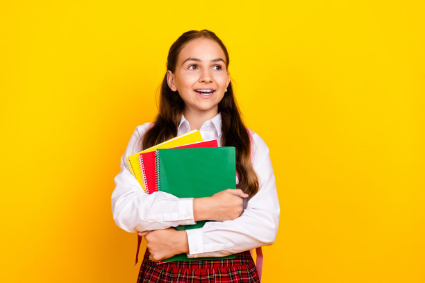 照片肖像可爱的十几岁的女学生勤奋地拿着课本，看起来空空荡荡，穿着时髦的制服孤立在黄色的背景图片下载