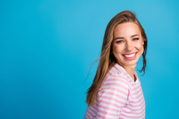照片肖像迷人的年轻女子飘动的头发微笑穿着时尚的条纹粉红色的衣服孤立的蓝色背景图片下载