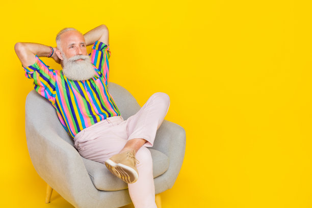 宁静英俊的人坐在扶手椅上的肖像，双手在头后，在黄色的背景上看起来空荡荡的图片下载